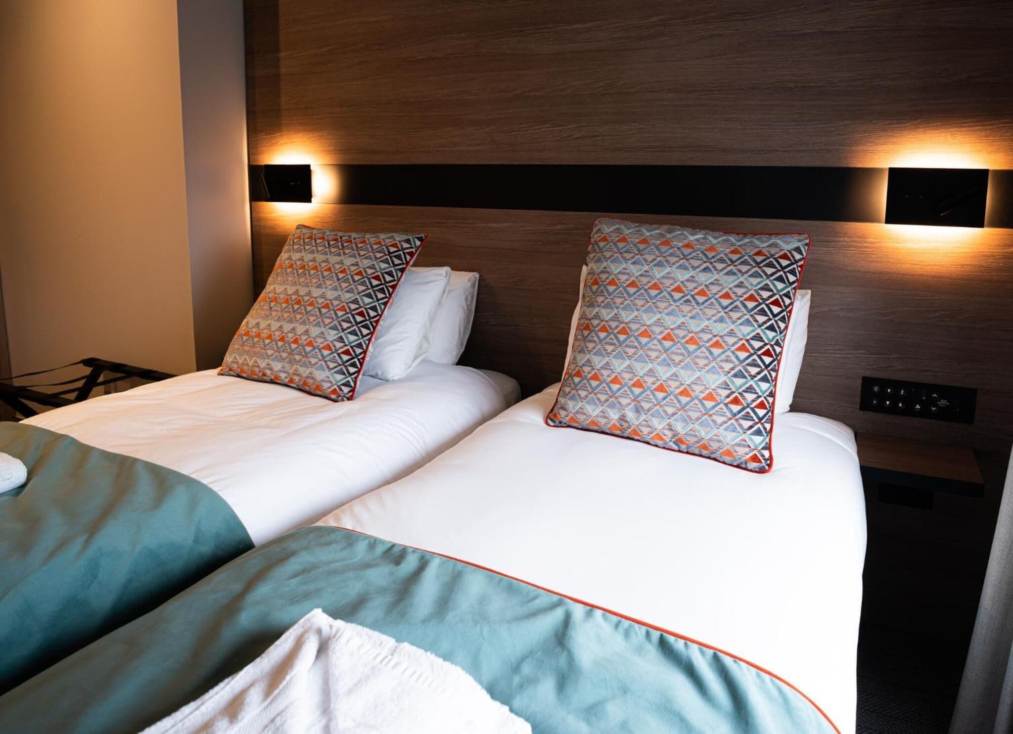 Une chambre d’hôtel avec deux lits, chacun agrémenté d’oreillers à motifs et d’une tête de lit en bois.