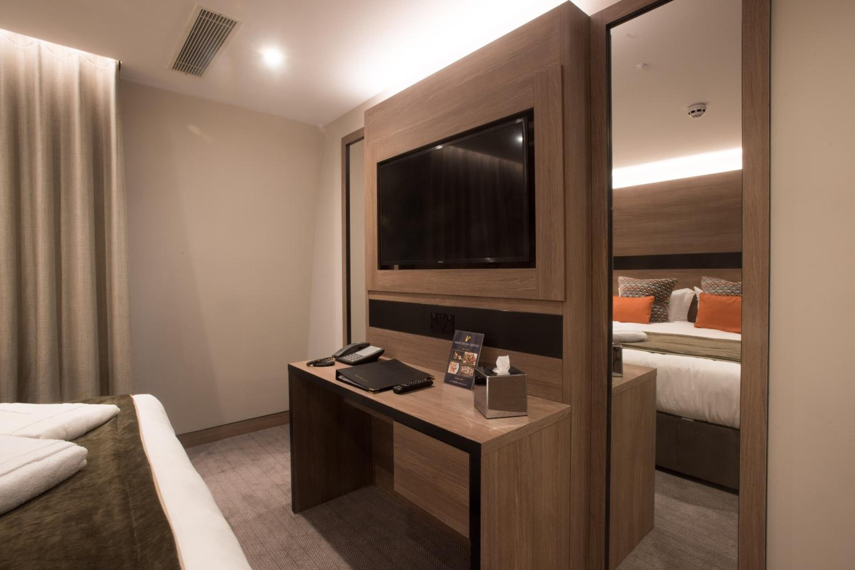 Ein Hotelzimmer mit Holzschreibtisch, Flachbildfernseher, Telefon, Notizblock und Taschentuchbox.