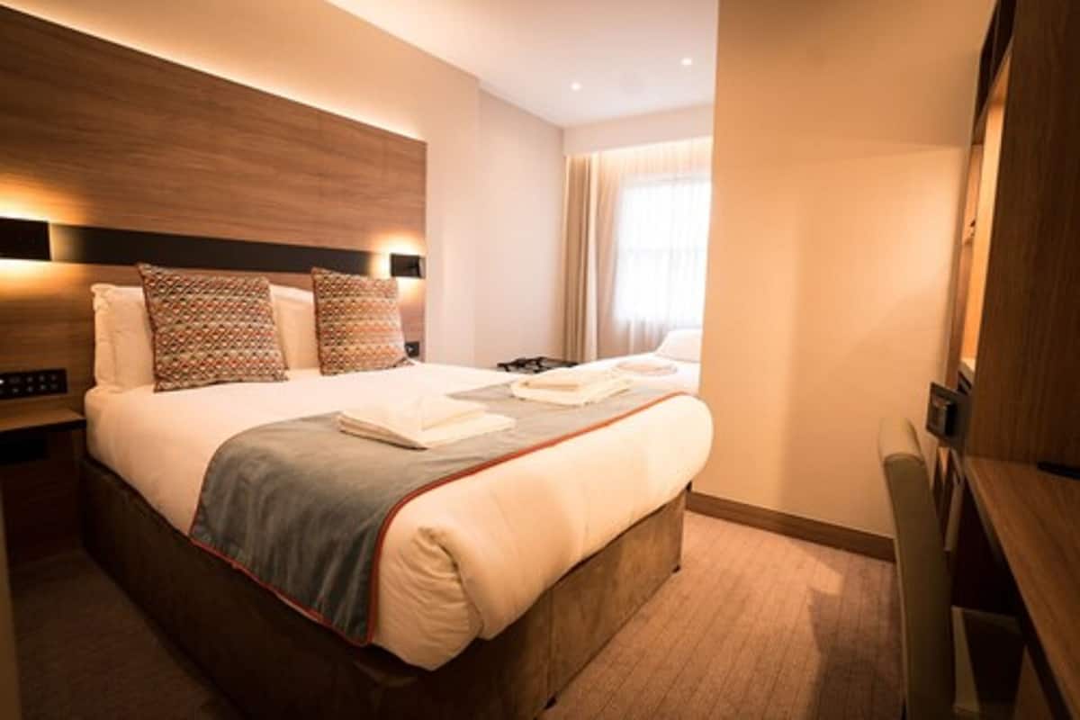 A modern hotel room with a large bed, a wooden headboard, and a flat-screen TV.