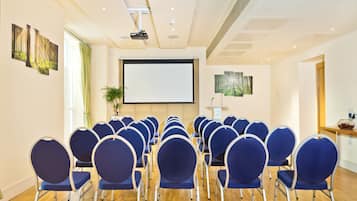 A conference room with rows of blue chairs, a projector screen, and a presentation podium.