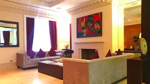 A spacious living room with a beige sofa, a smaller sofa, and a coffee table. There is a fireplace and a large abstract painting on the wall. - The Park City Grand Plaza Kensington (London)