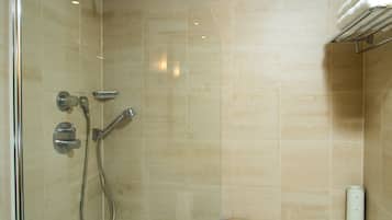 A modern bathroom with beige tiles, a glass shower enclosure, a bathtub, and a towel rack.