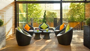 A modern outdoor seating area with wicker furniture and a glass enclosure. - The Park City Grand Plaza Kensington (London)