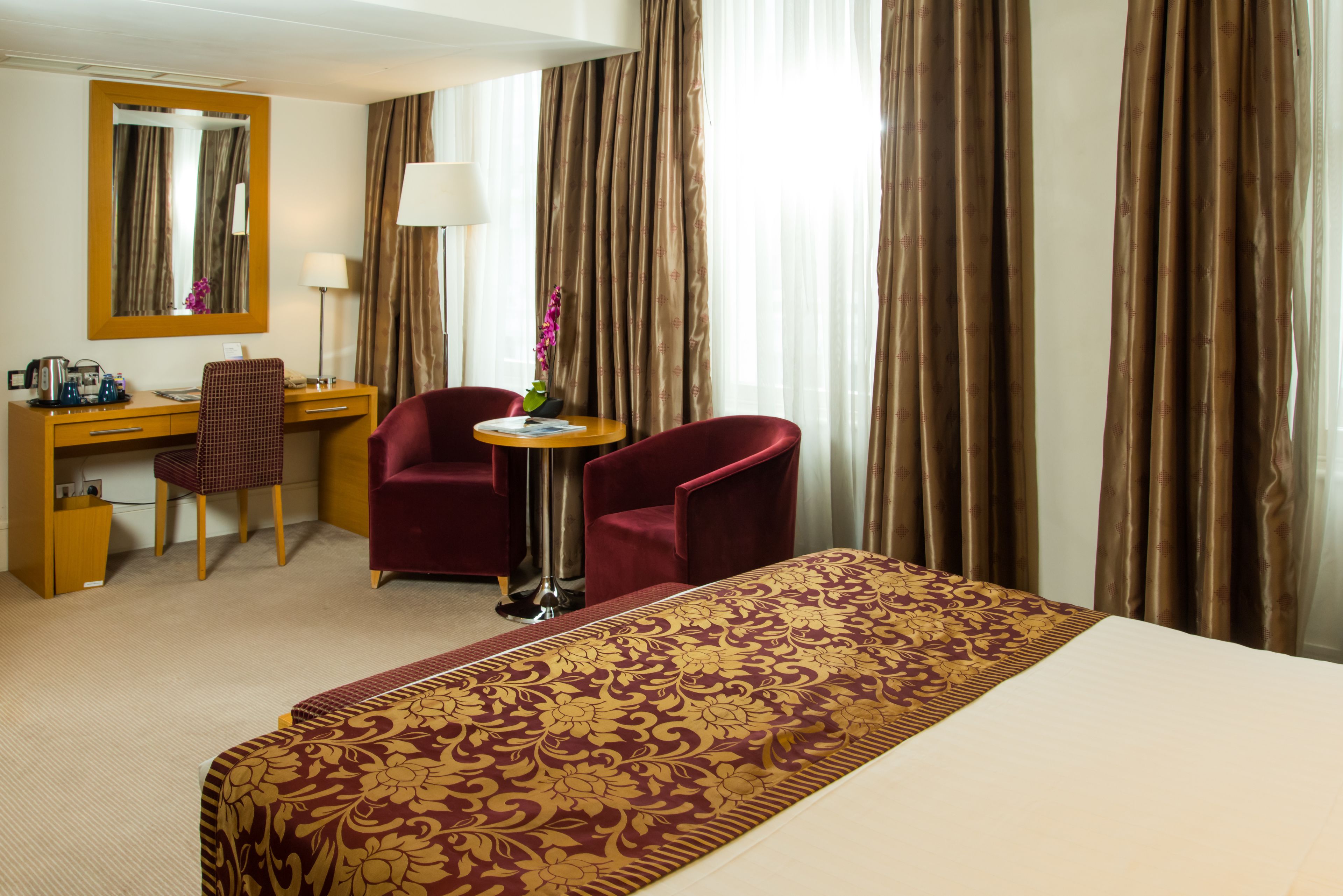 Una habitación de hotel con una cama grande, un escritorio con silla, una lámpara y un espejo.