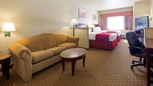 Een hotelkamer met een bank, een klein tafeltje, een bed met een rode sprei, een bureau met een computer en een televisie.