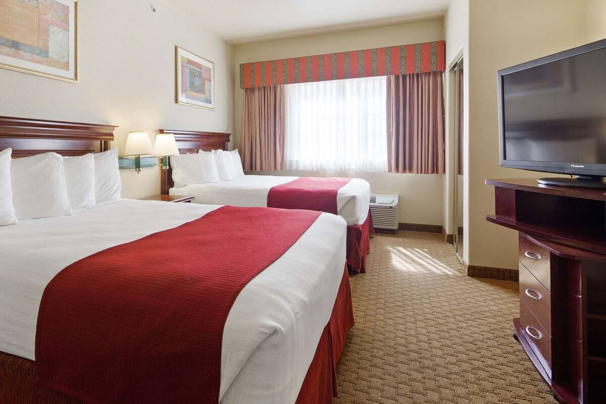 Une chambre d’hôtel avec deux lits, une télévision et une fenêtre avec des rideaux.