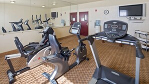 Een fitnessruimte met diverse fitnessapparaten, een waterdispenser, een klok en een televisie.