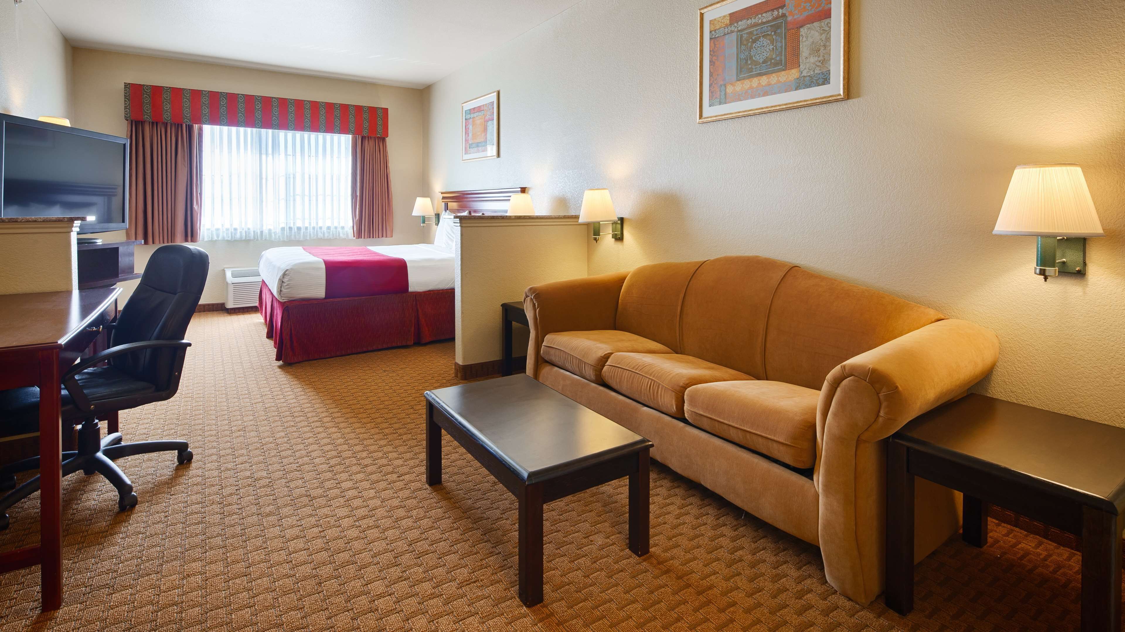 A hotel room with a bed, a sofa, a desk, a chair, and two wall lamps.