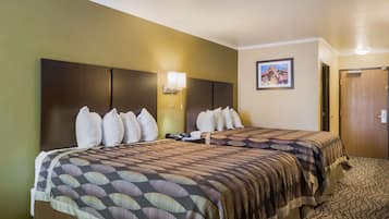 A hotel room with two beds, a headboard, a wall-mounted lamp, and a framed picture.