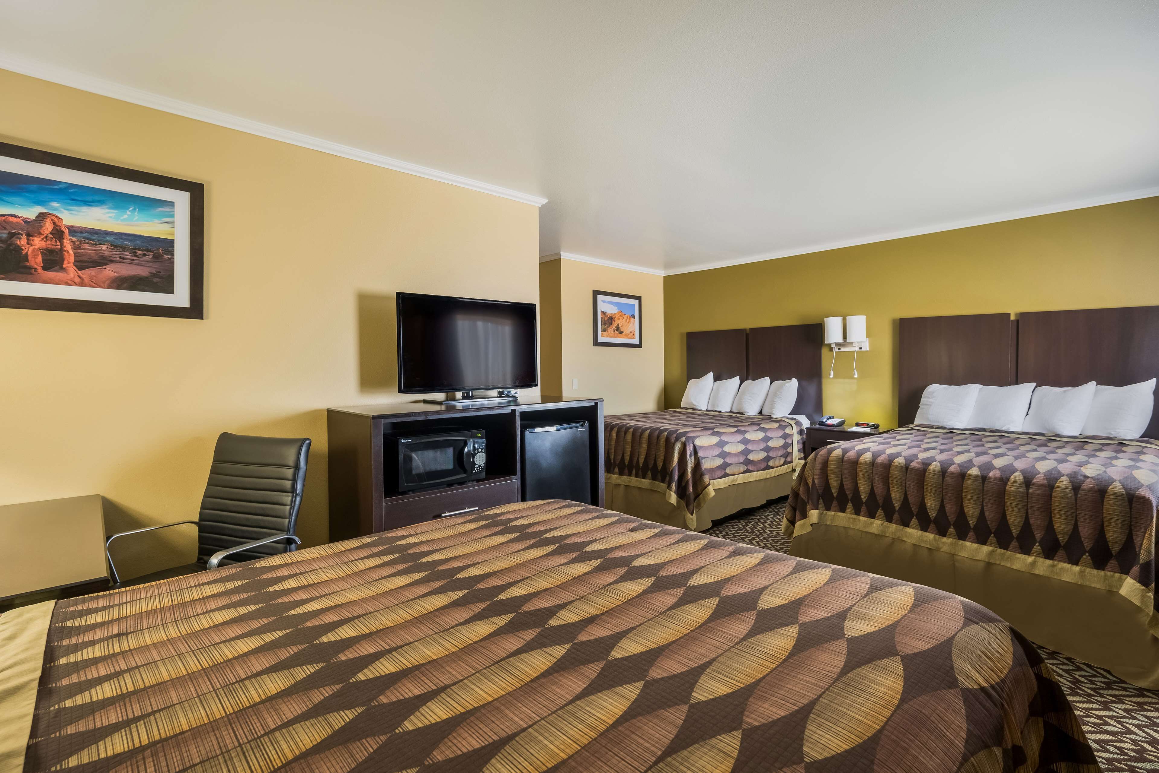 A hotel room with two beds, a TV, a desk with a computer, and a chair.