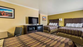 A hotel room with two beds, a TV, a desk with a computer, and a chair.