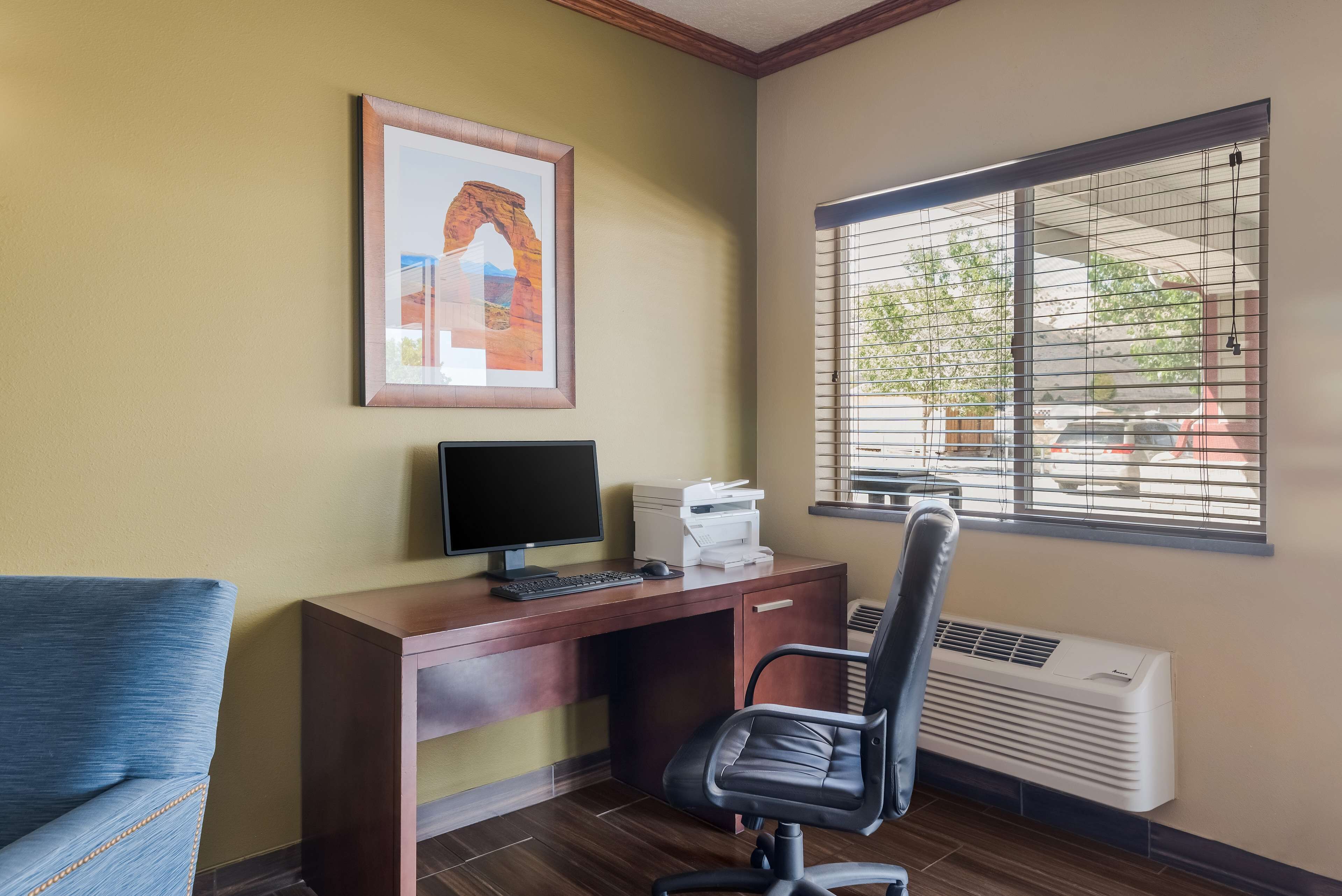A room with a desk, computer, printer, chair, and an air conditioner.