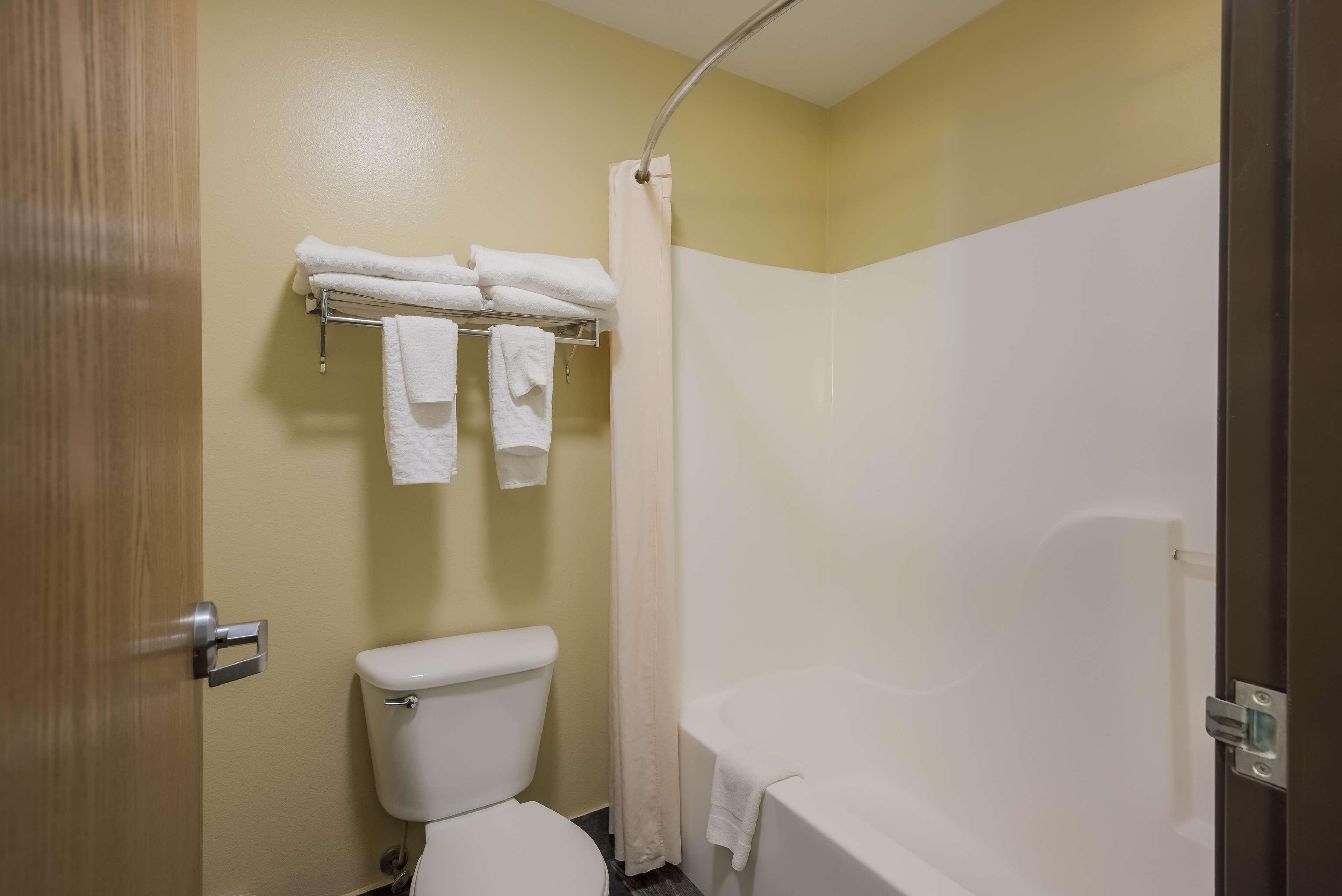 A bathroom with a toilet, a shower with a curtain, and a towel rack with folded towels.