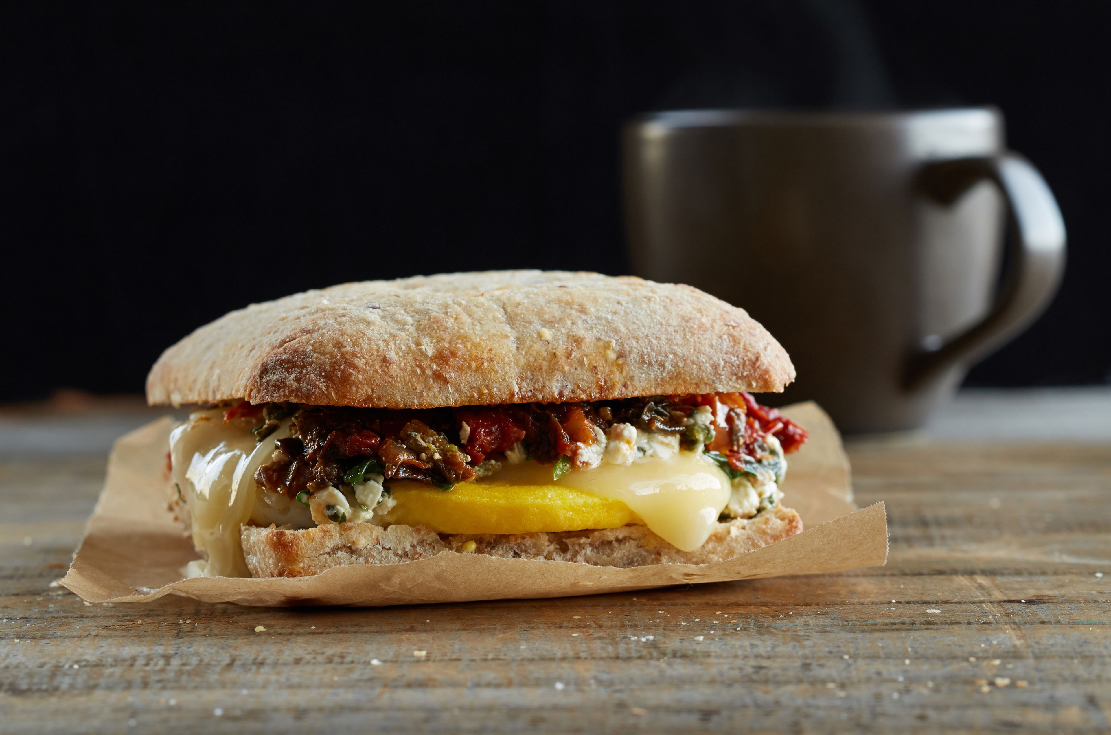 Un sandwich sur une feuille de papier, avec une tasse en arrière-plan.