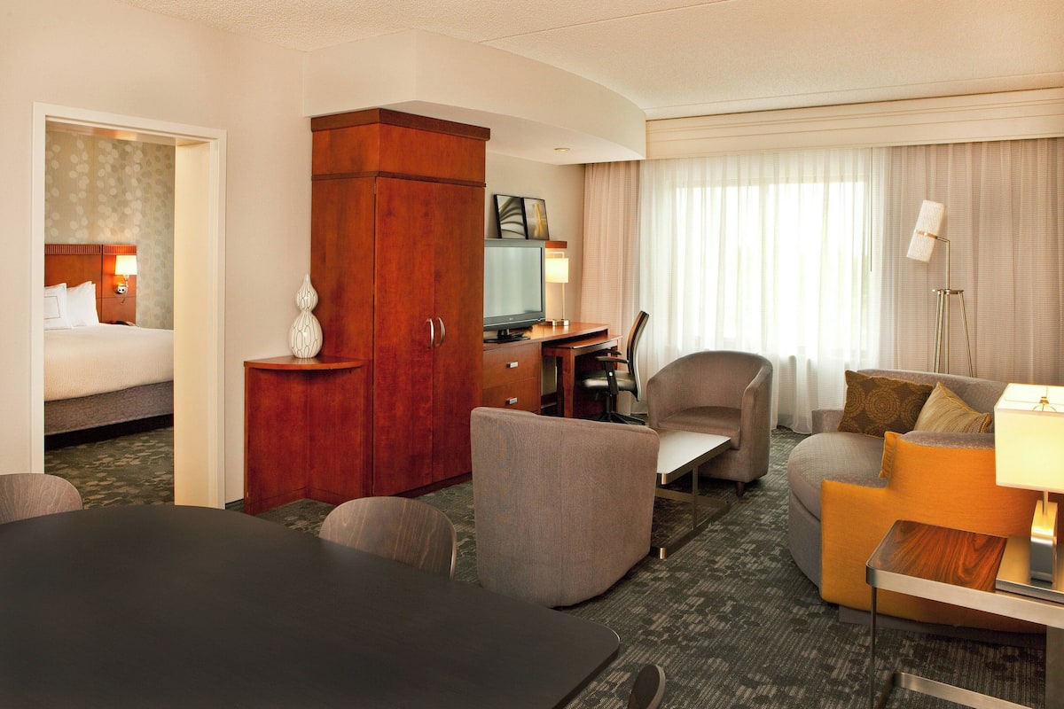 A hotel room with a bed, a desk, a chair, a sofa, and a lamp.