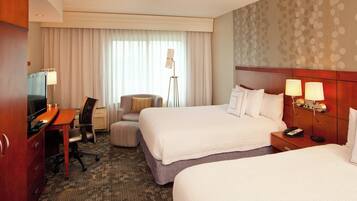 A hotel room with two beds, a desk with a TV, a chair, a lamp, and a bedside table with a phone.