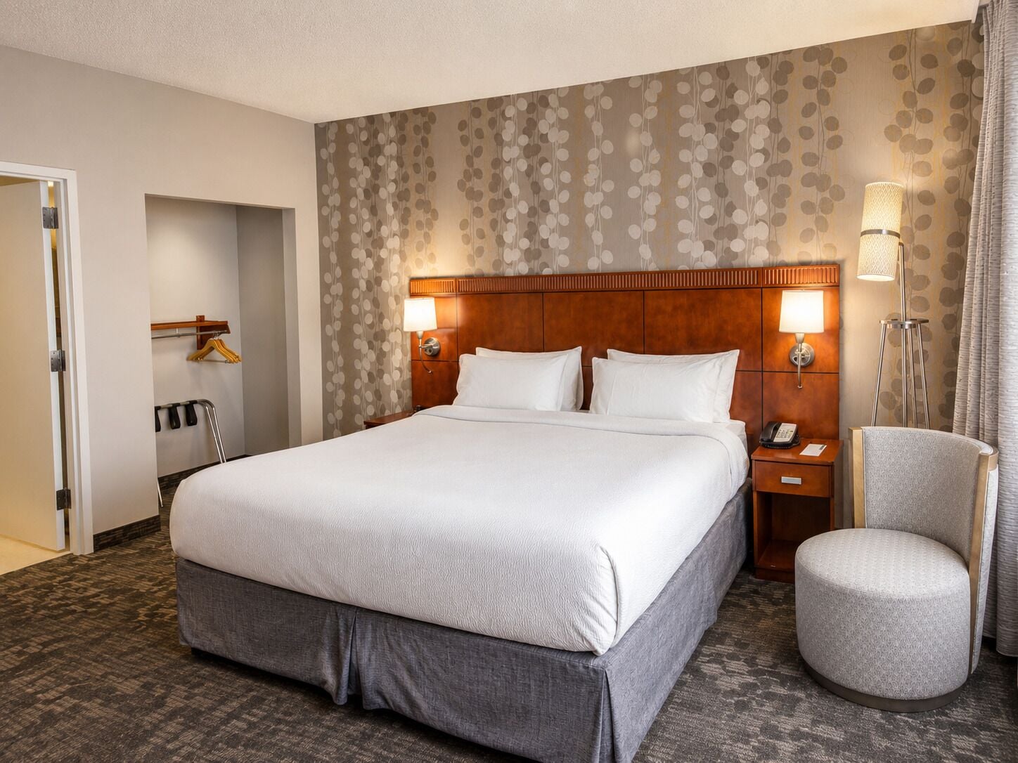 Een hotelkamer met een groot bed, een nachtkastje met lamp, een stoel en een kledingkast.