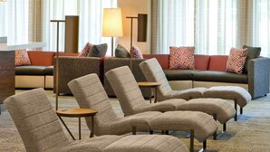 Un vestíbulo de hotel con zona de estar que incluye sofás y sillones, una lámpara y un amplio ventanal con cortinas.