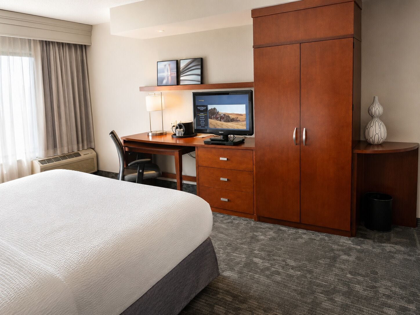 A hotel room with a bed, desk, computer, and wardrobe.