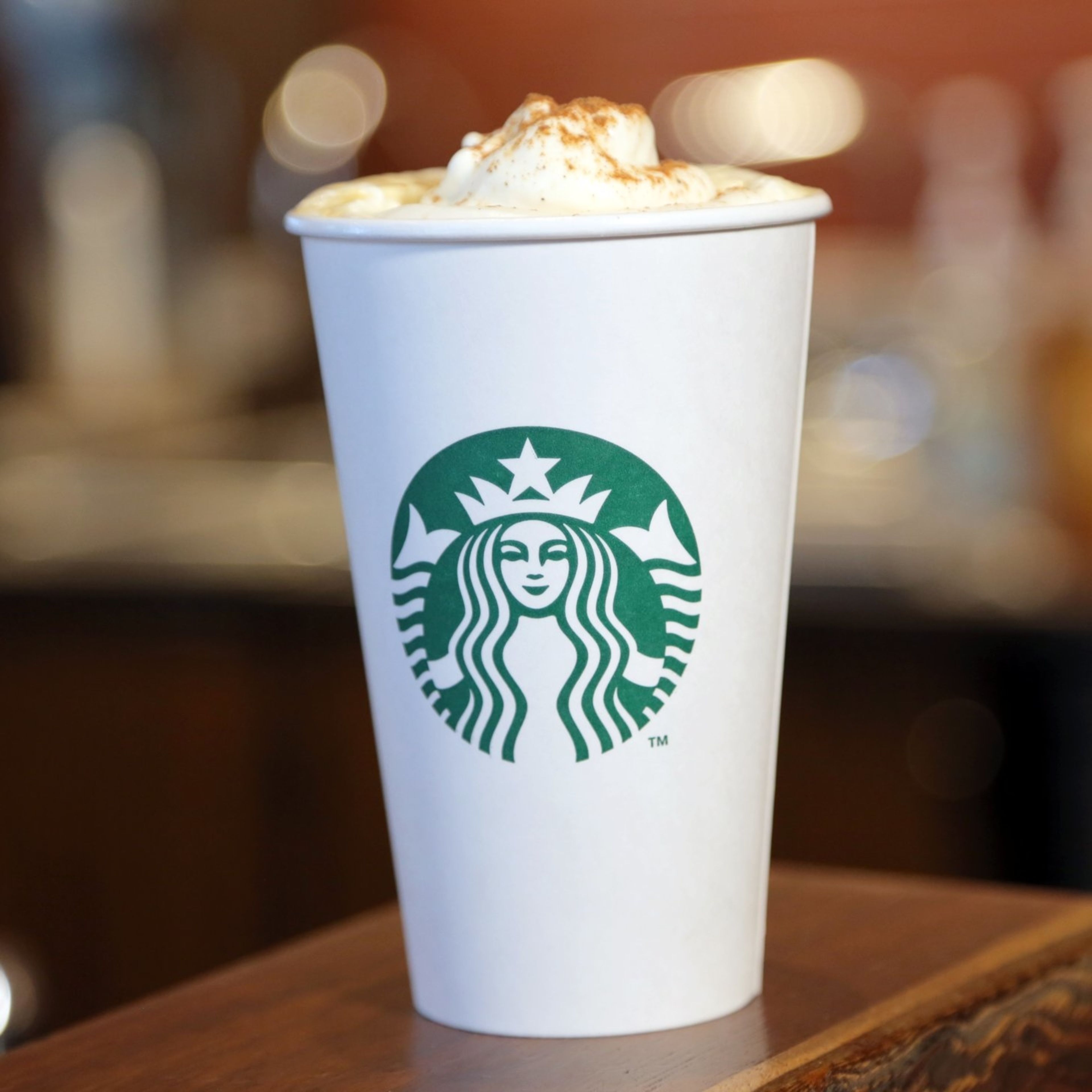 A Starbucks cup with a frothy beverage on a wooden surface.