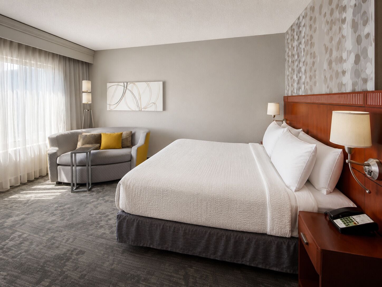 Habitación de hotel con una cama grande, un sofá, un escritorio con teléfono y una pared con diseño decorativo.