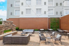 An outdoor patio area with a stone fire feature, seating, and tables. - Hilton Garden Inn Buffalo Airport (Buffalo)