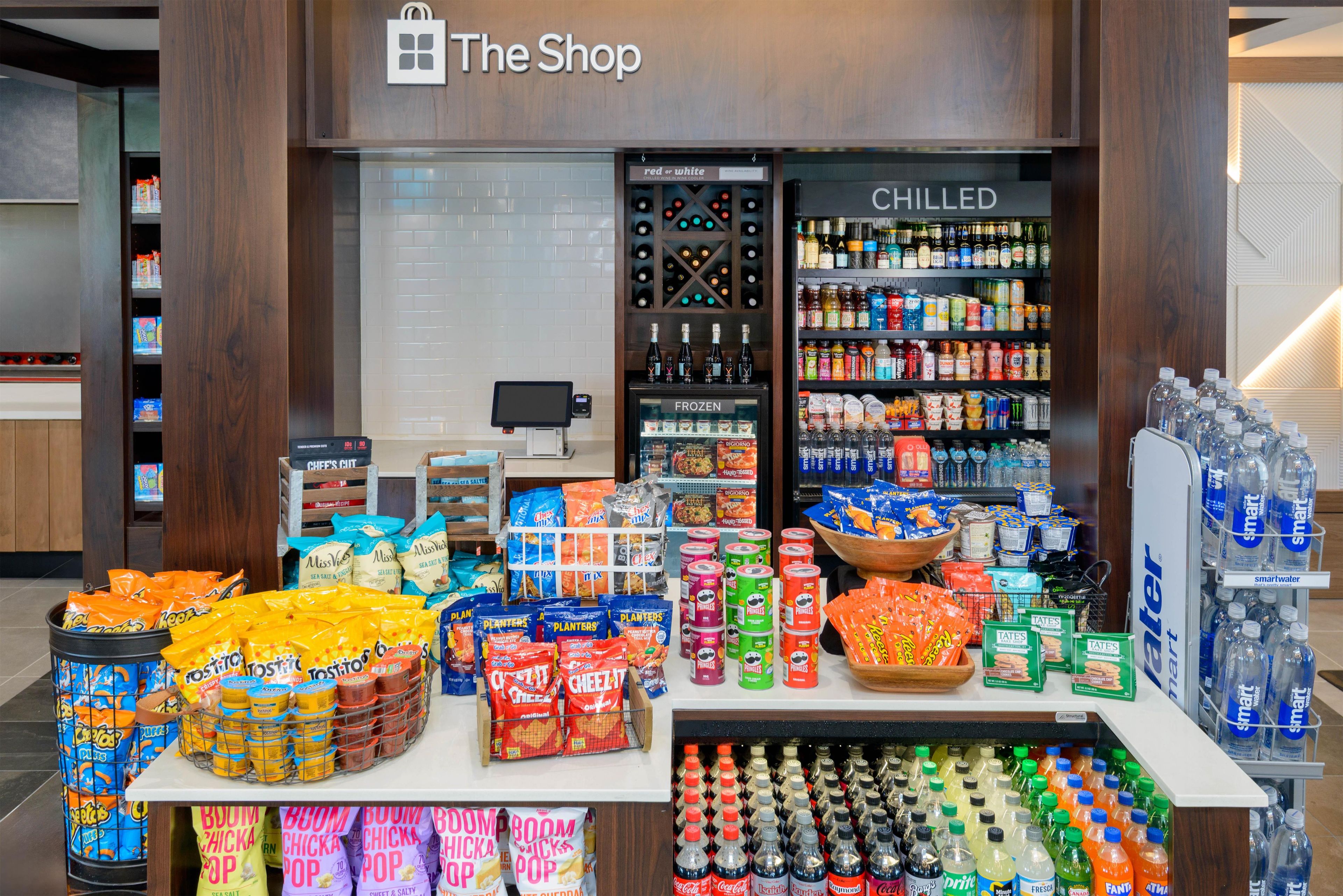 A snack display with various chips and snacks, a chilled beverage section, and a counter with a cash register.