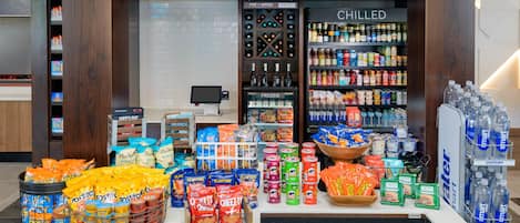 Mostrador con una selección de papas fritas y otros bocadillos, una sección de bebidas frías y una caja registradora.