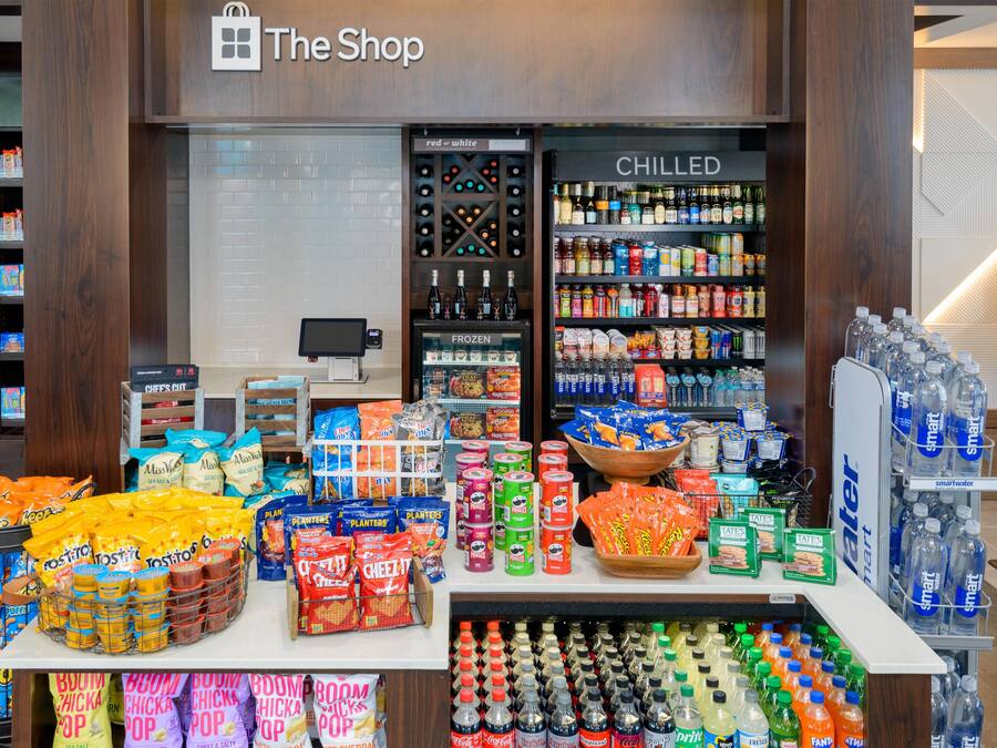 A snack display with various chips and snacks, a chilled beverage section, and a counter with a cash register.