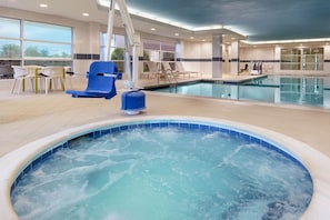 Una piscina interior con un jacuzzi, sillones de descanso y una cama solárium.