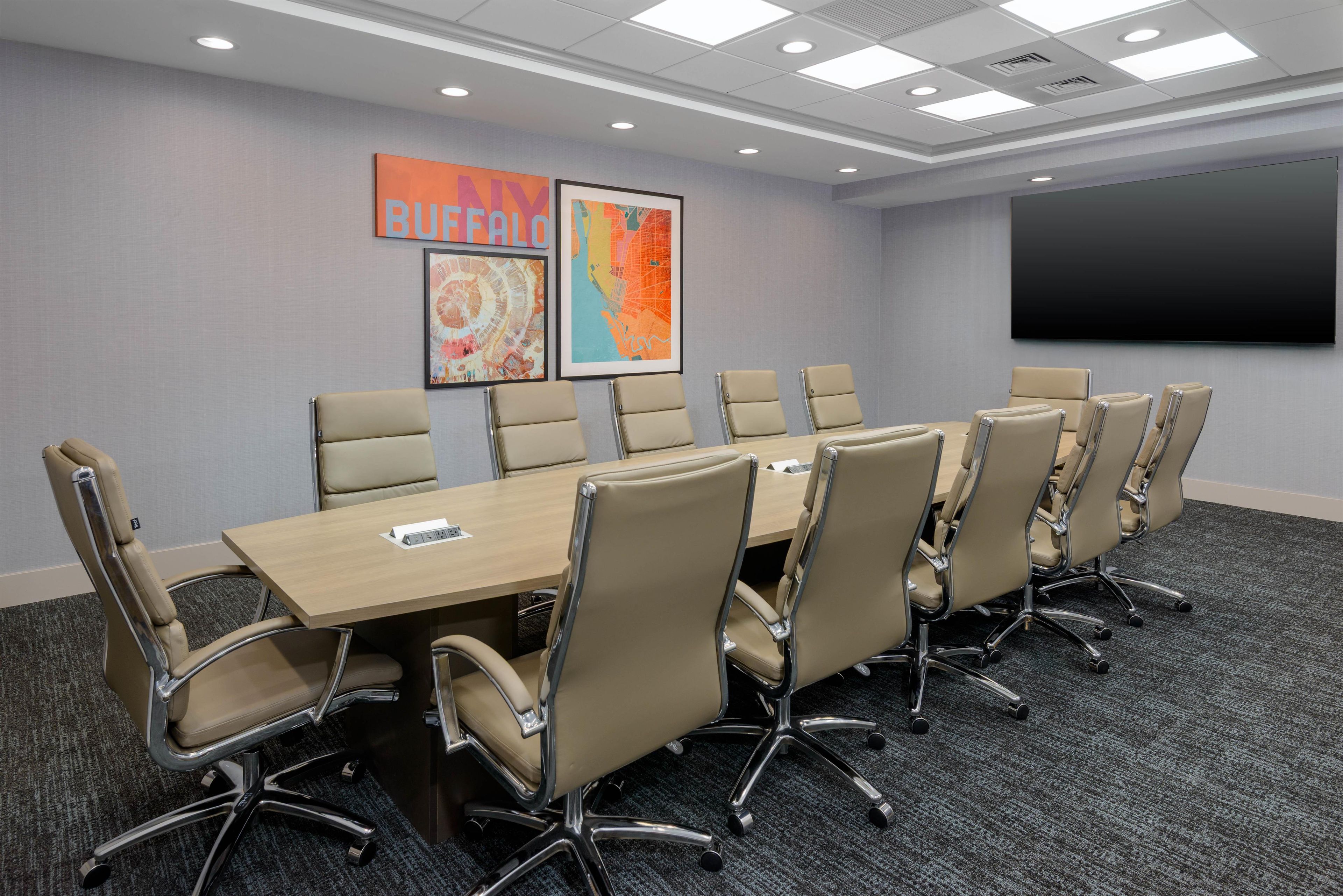 A conference room with a long table and chairs, a projector screen, and artwork on the wall.