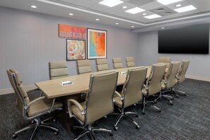 Un salón de conferencias con una larga mesa y sillas, una pantalla de proyector y obras de arte en la pared.