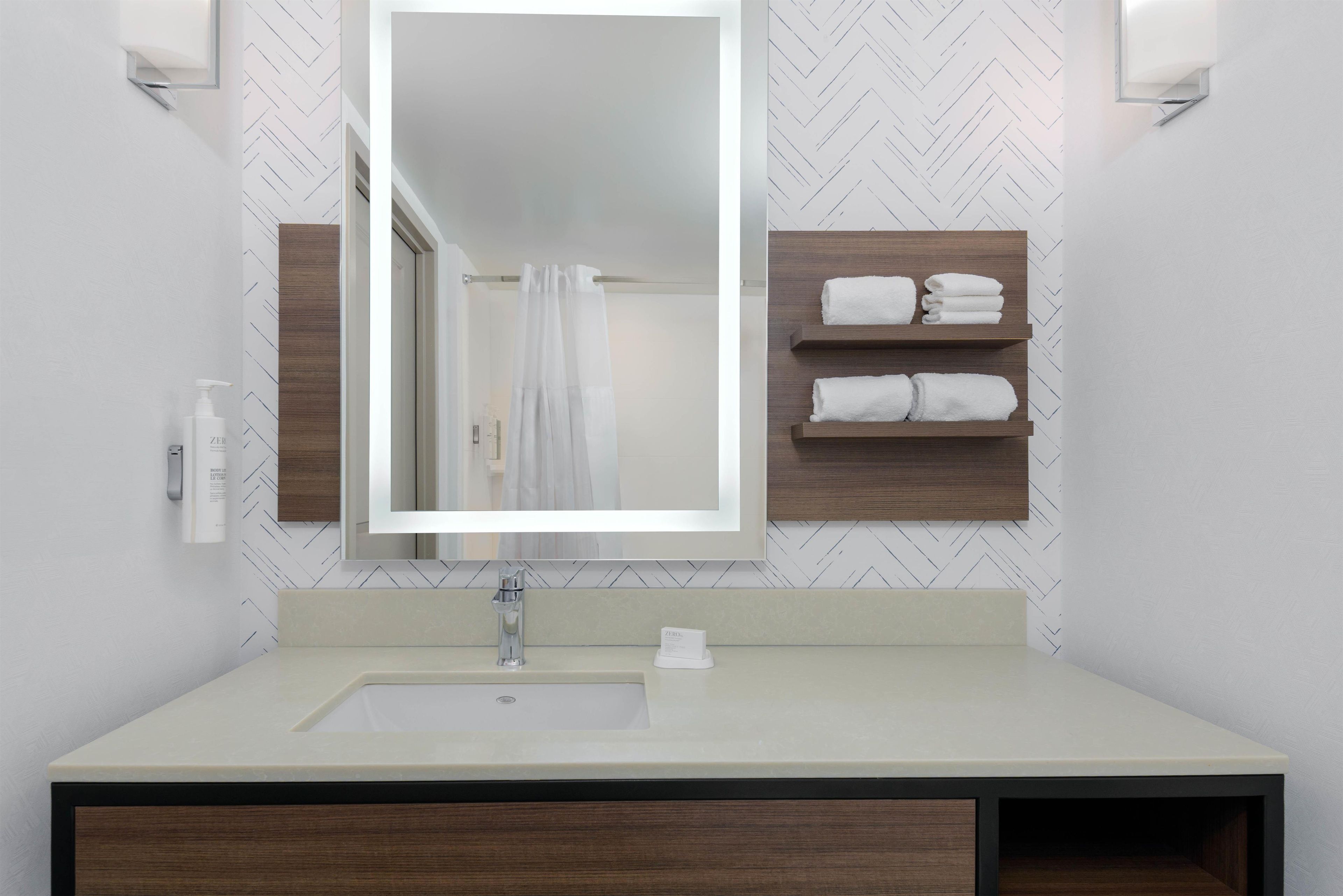 A bathroom with a large mirror, a sink, a towel rack, and a shower curtain.