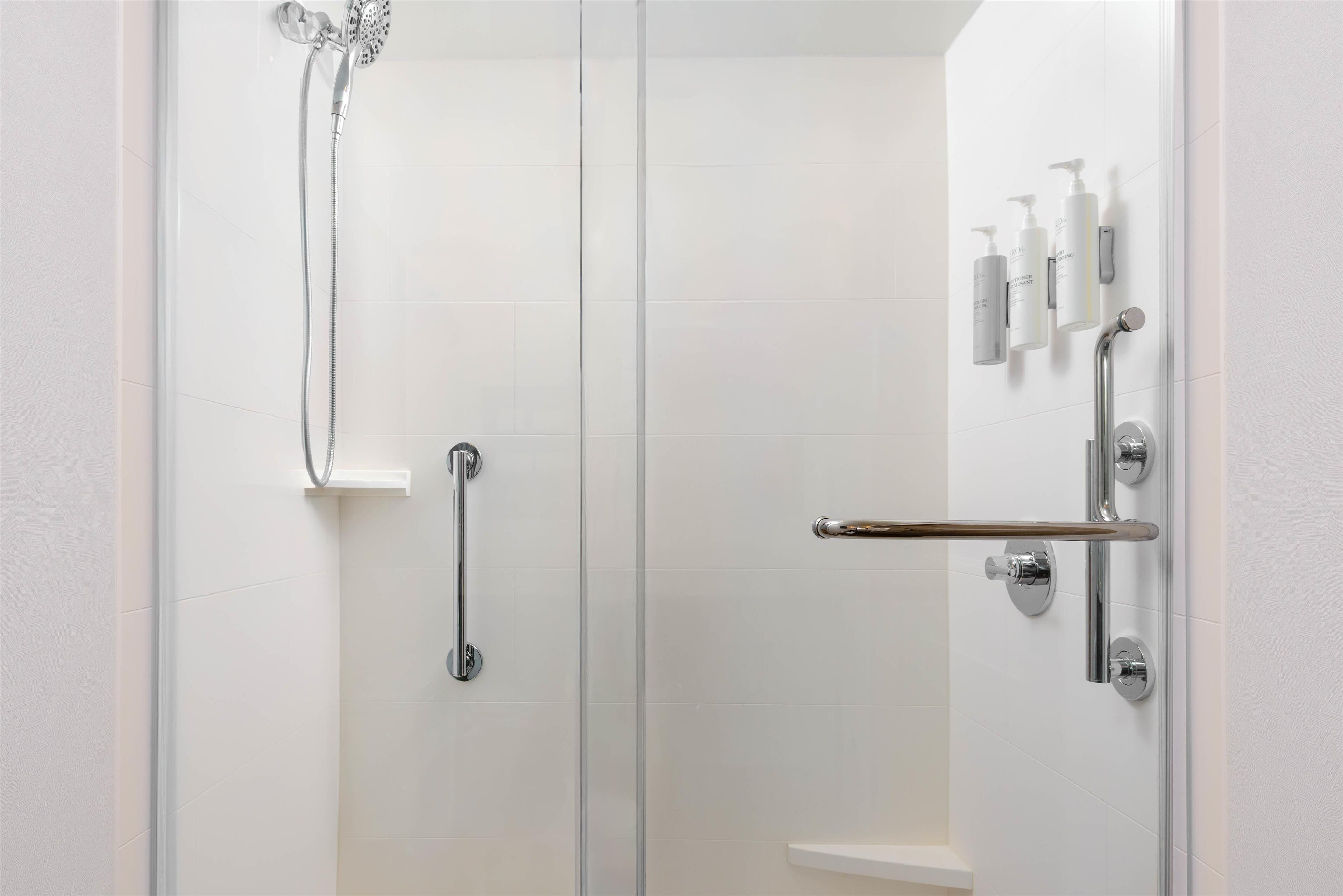 A modern bathroom with a glass shower enclosure, a grab bar, and a shelf with toiletries.