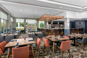 A hotel restaurant with multiple tables, chairs, and a bar area. - Hilton Garden Inn Buffalo Airport (Buffalo)