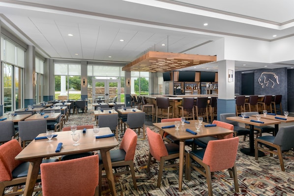 Un restaurante de hotel con varias mesas, sillas y una zona de bar.