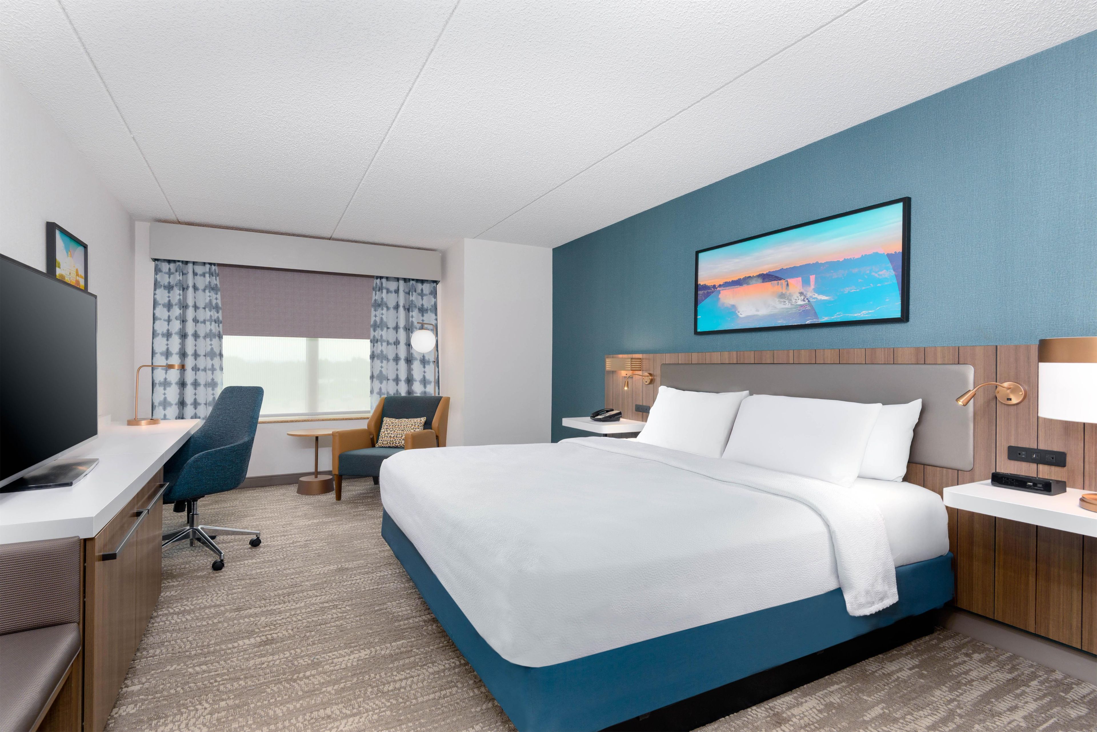 A hotel room with a bed, desk, chair, and a TV.