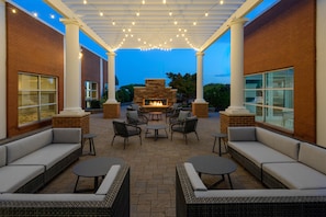An outdoor patio area with brick walls, white columns, and a fire pit surrounded by wicker furniture. - Hilton Garden Inn Buffalo Airport (Buffalo)
