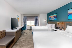Ein Hotelzimmer mit Fernseher, Schreibtisch, Stuhl, zwei Betten, einer Schreibtischlampe und Bildern an den Wänden.