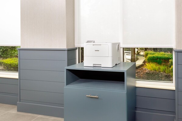 Una impresora sobre un mueble gris, con vista al jardín desde una ventana.