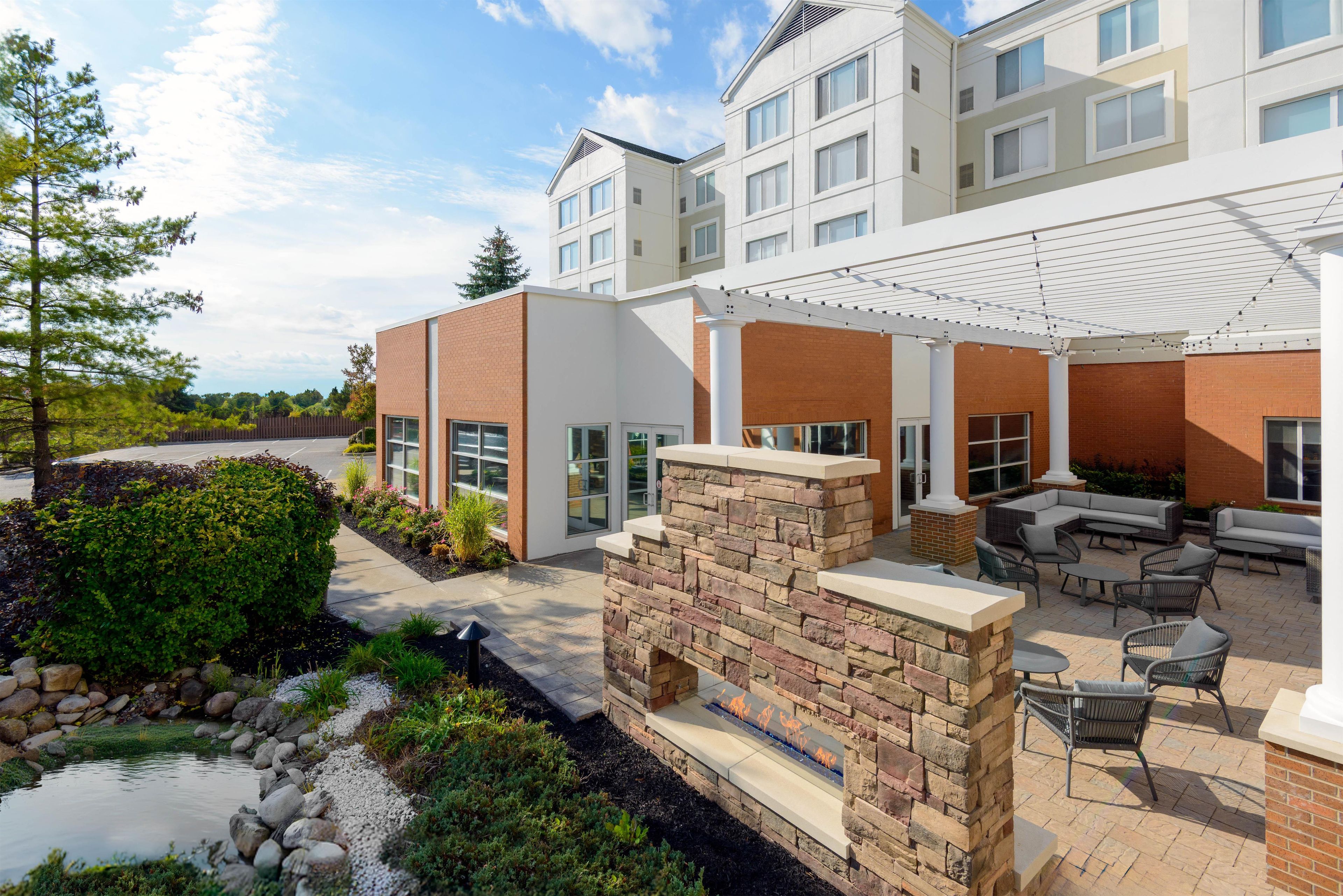 A modern building with a covered patio area, outdoor seating, and a small water feature.