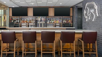 A bar area with a modern design, featuring a counter with multiple taps and shelves of bottles. There are four bar stools in front of the counter.