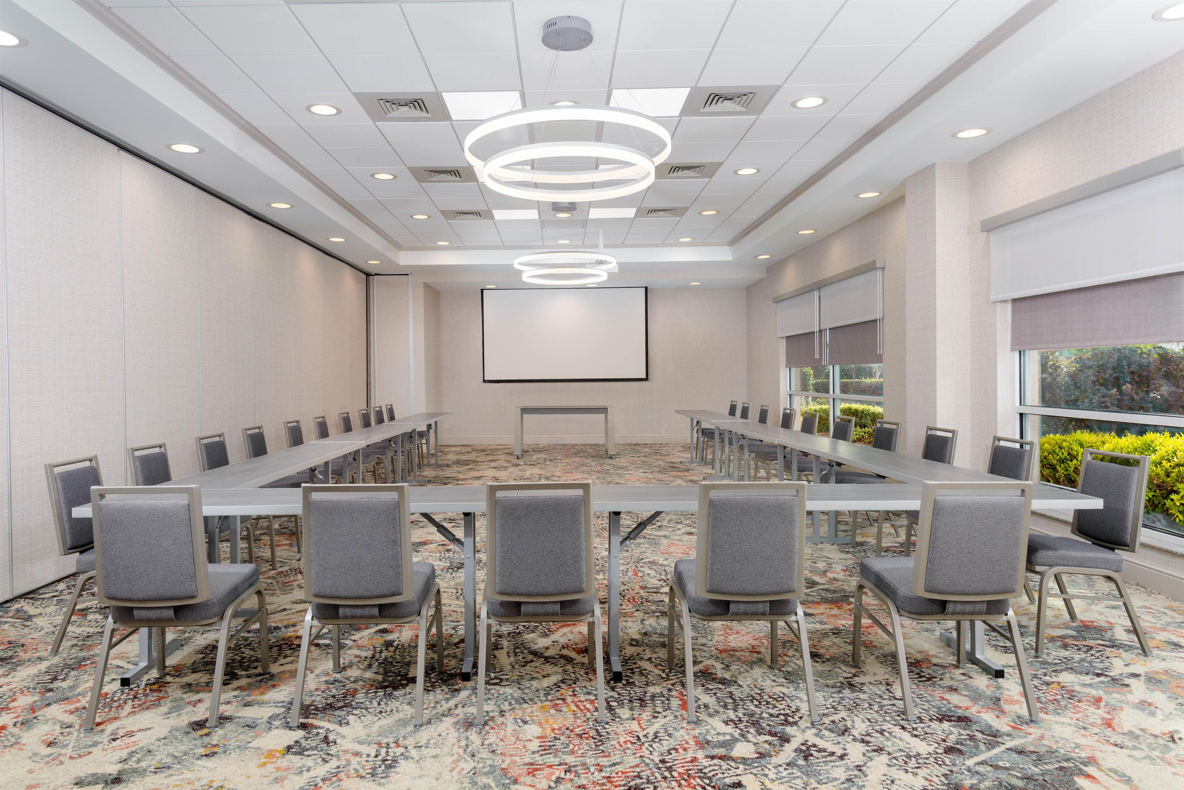 A conference room with a long table and chairs, a projector screen, and a patterned carpet.