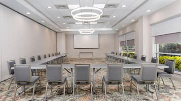 A conference room with a long table and chairs, a projector screen, and a patterned carpet.