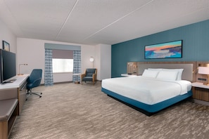 Una habitación de hotel con una cama grande, un escritorio con silla, un televisor, una mesita con silla y un cuadro en la pared.