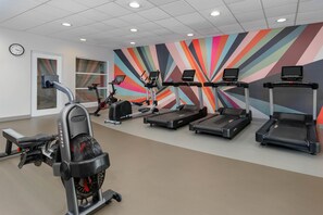 A gym with treadmills, an elliptical, and a stationary bike, featuring a colorful wall mural.