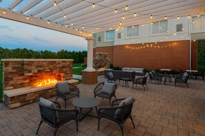 Un espacio de patio al aire libre con chimenea de piedra, mobiliario de mimbre y luces colgantes.