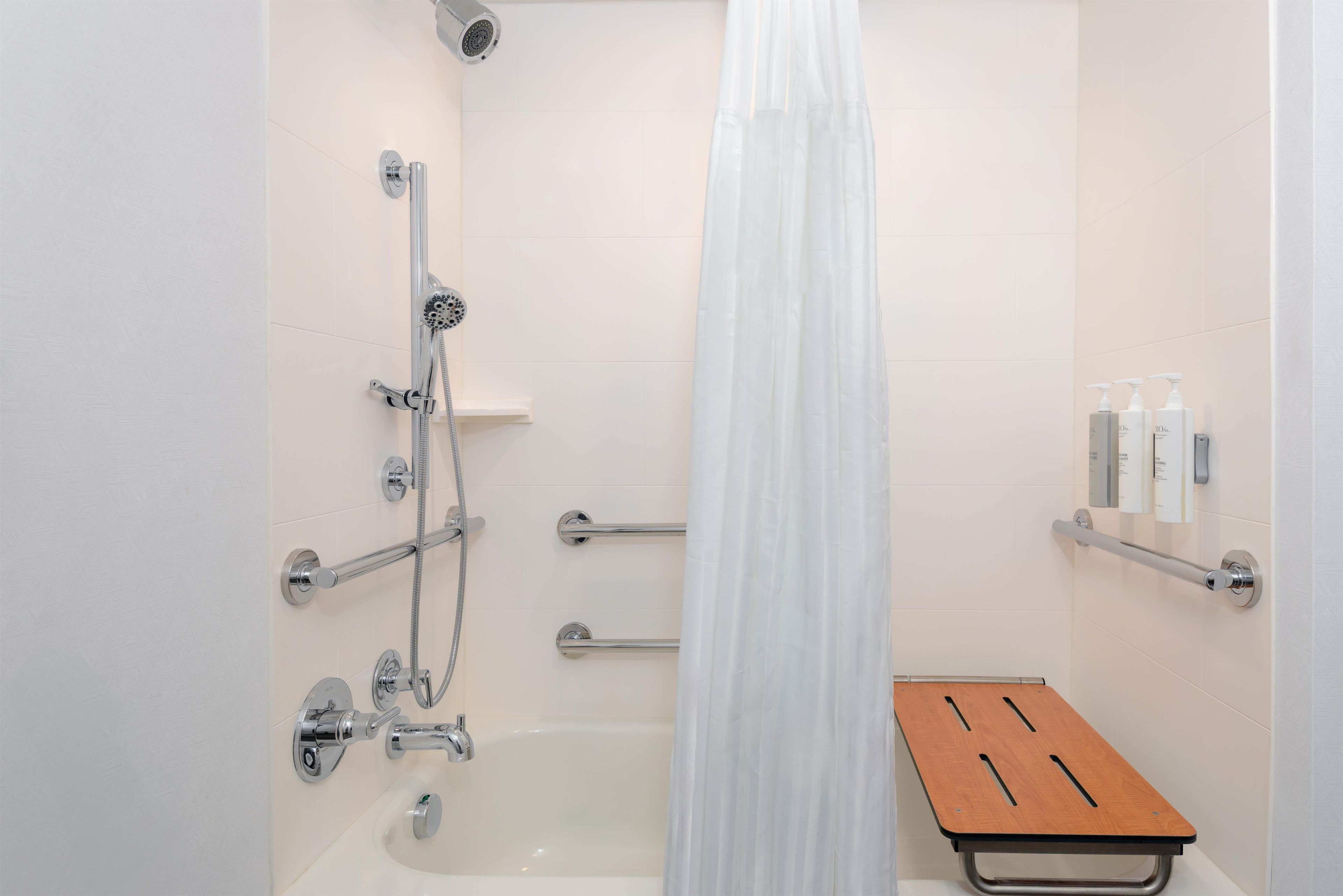 A shower area with a bathtub, a showerhead, a handheld shower, a glass shower enclosure, and a wooden bench.