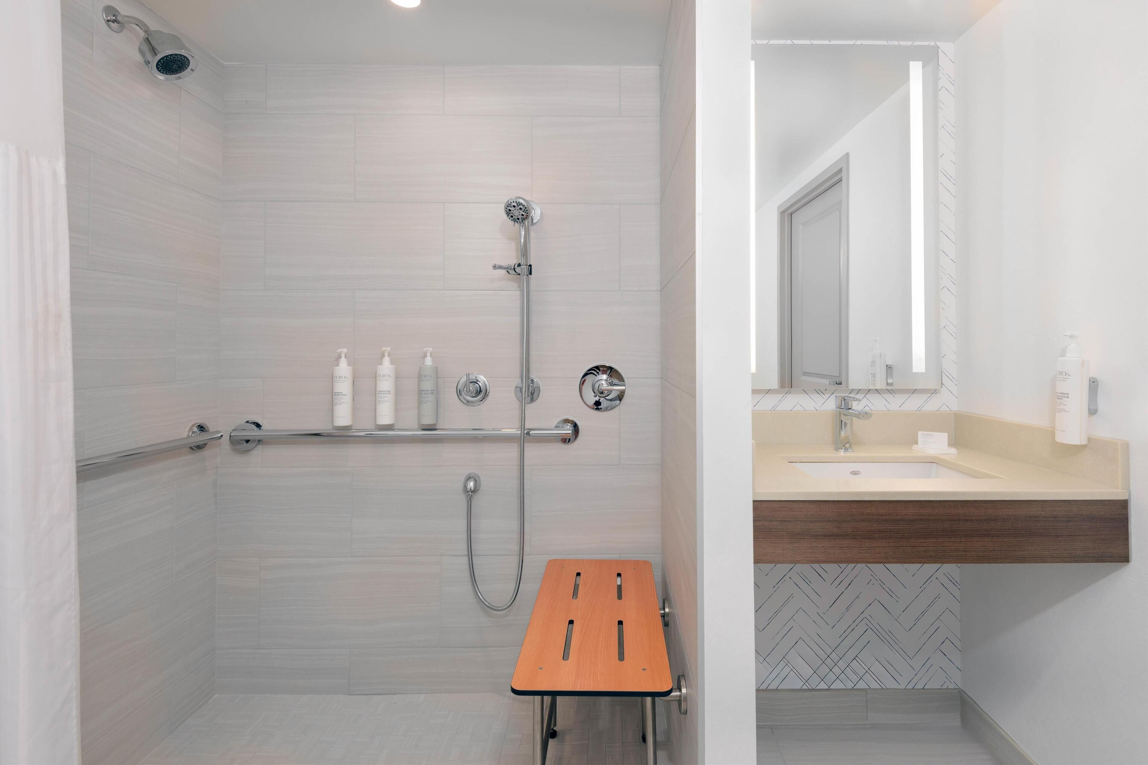 Une salle de bain moderne avec une douche, un meuble-lavabo avec un miroir et un tabouret en bois.