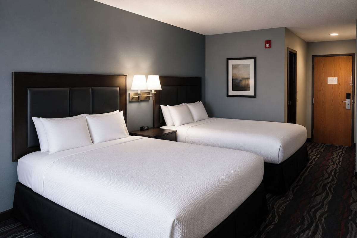 A hotel room with two beds, a nightstand with a lamp, a framed picture on the wall, and a door with a lock.